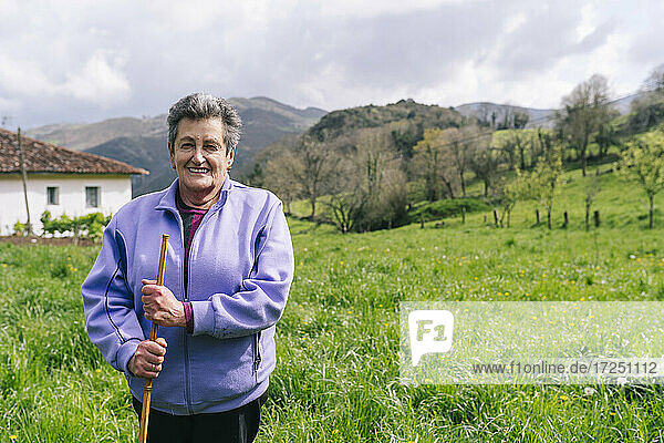 Smiling active senior woman standing with walking cane on grass