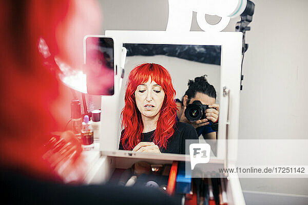 Mann fotografiert weibliche Vloggerin beim Filmen vor dem Spiegel im Studio