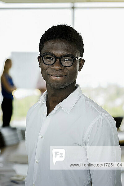 Junger männlicher Unternehmer mit Brille lächelt im Büro