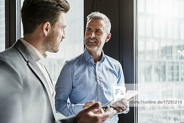 Älterer männlicher Unternehmer  der ein digitales Tablet hält und mit einem Kollegen in einer Besprechung im Büro diskutiert
