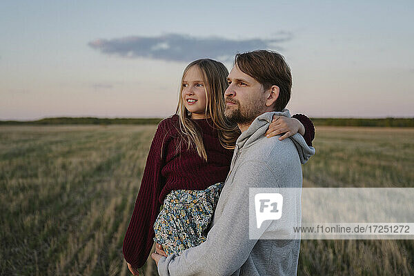 Vater mit Tochter in einem Feld stehend und Sonnenuntergang beobachtend