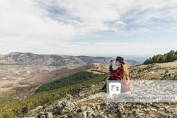 Junge Frau mit Hut  die in den Ferien auf einem Berg sitzt und nachdenkt