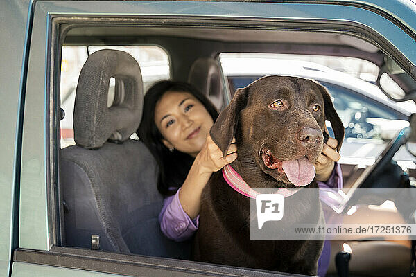Mittlere erwachsene Frau sitzt mit Hund und schaut durch ein Fenster im Auto