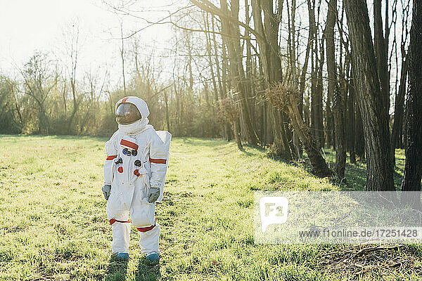 Female explorer wearing space suit standing in forest on sunny day