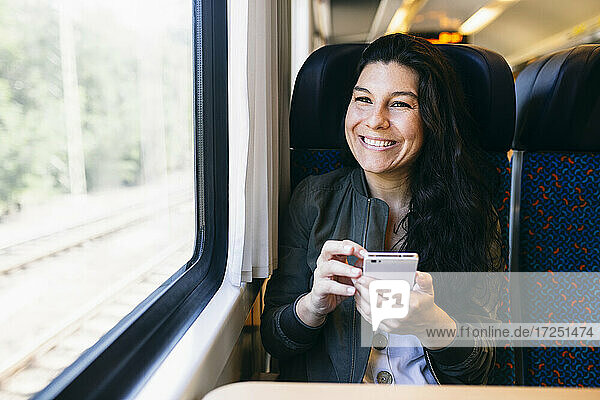 Woman with mobile phone looking through window while sitting in train
