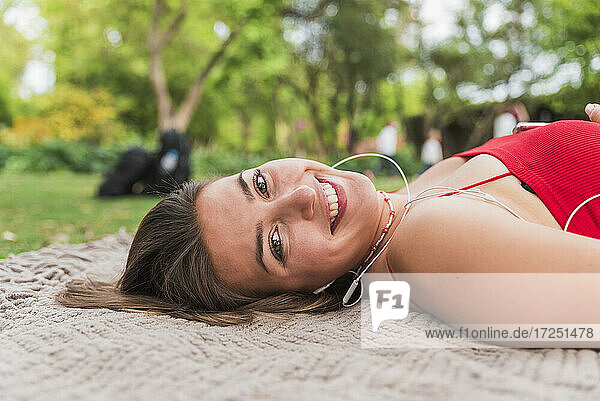 Glückliche junge Frau auf einer Decke im Park liegend