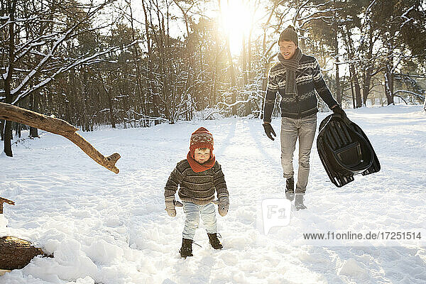 Vater mit Schlitten geht im Winter auf Schnee auf seinen Sohn zu