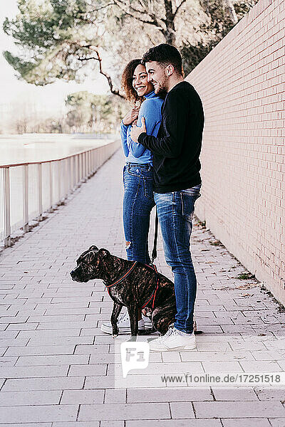 Young couple standing together with dog on footpath