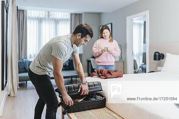 Mid erwachsenen Mann Auspacken von Gepäck auf dem Bett mit Frau im Hintergrund im Hotel