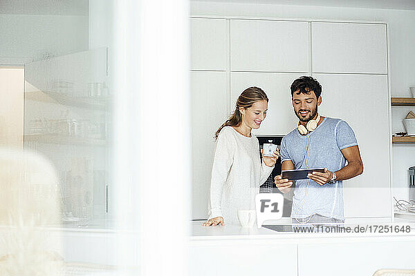 Lächelndes junges Paar  das in der Küche stehend über ein digitales Tablet diskutiert