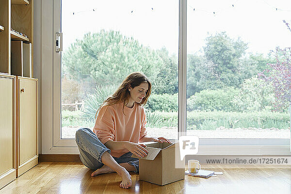 Schöne Frau beim Öffnen eines Kartons  während sie zu Hause sitzt