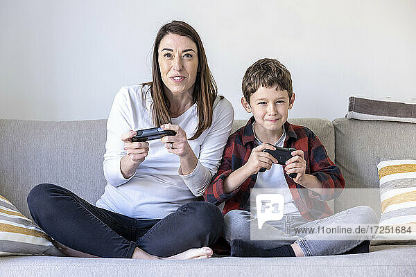 Excited woman and son playing video game while sitting on sofa in living room