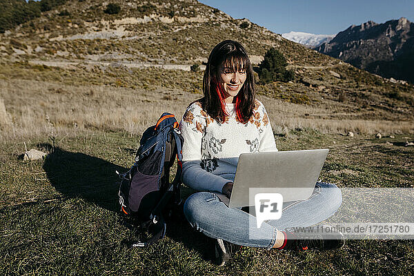 Aufgeregte Frau  die einen Laptop benutzt  während sie im Gras auf einem Berg sitzt