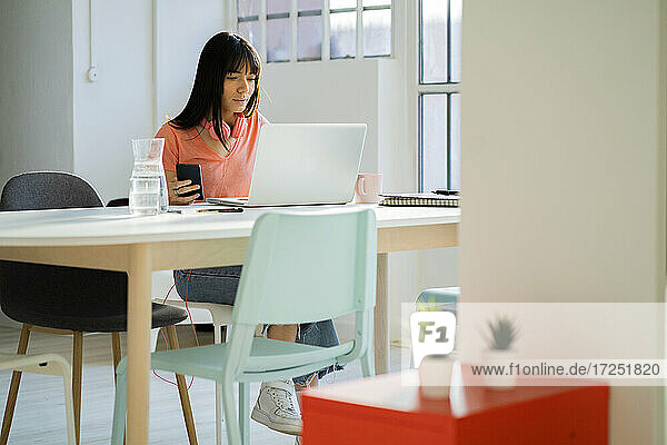 Businesswoman with smart phone using laptop at home office