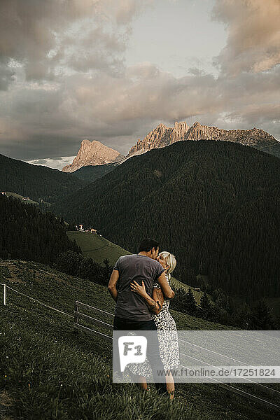 Couple embracing while standing on grass near dolomites moutain ranges in South Tyrol  Italy