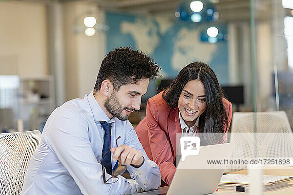 Smiling male and female professionals discussing over laptop in coworking office