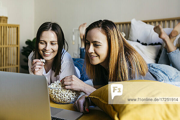 Smiling friends enjoying popcorn while watching movie in bedroom