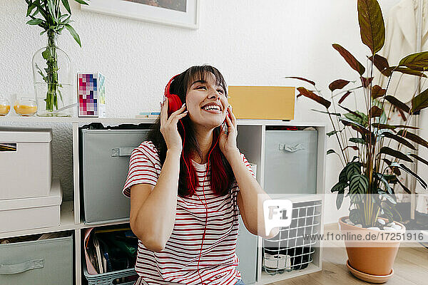 Lächelnde Frau hört Musik über Kopfhörer im Wohnzimmer