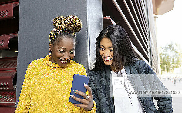 Multiethnische Freundinnen schauen auf ihr Smartphone an der Wand