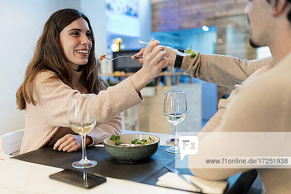 Couple feeding salad to each other at restaurant table