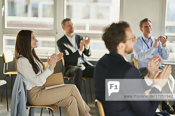 Businesswoman clapping hands with colleagues in education conference centre