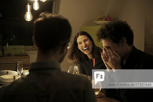 Reife Frau lacht mit männlichen Freunden während einer Feier zu Hause