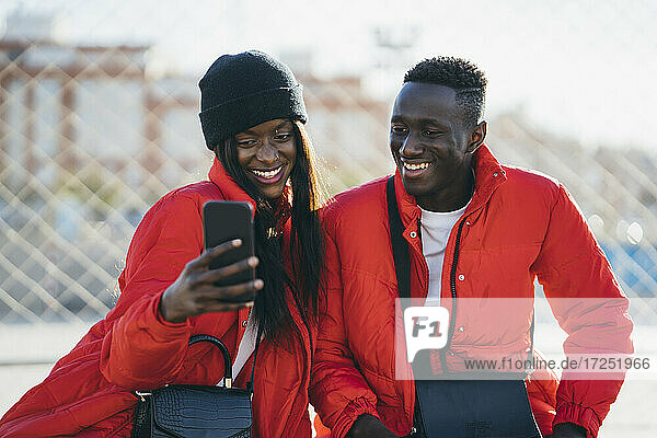 Glückliches Paar in roten Jacken benutzt Smartphone im Freien