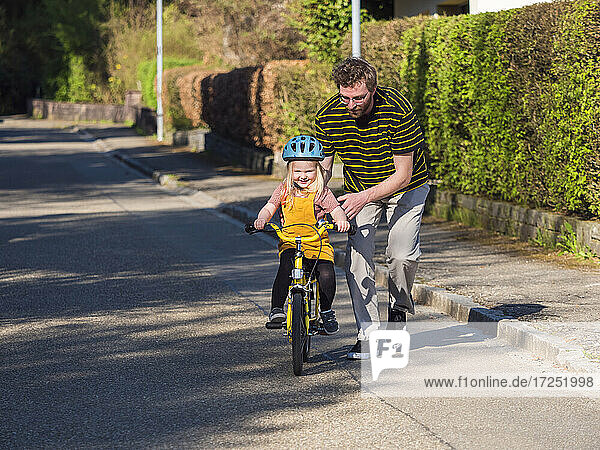 Vater bringt seiner Tochter in der Nähe des Gehwegs auf der Straße das Radfahren bei
