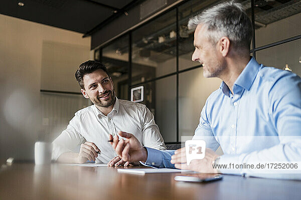 Lächelnde Geschäftsleute  die am Tisch im Sitzungssaal am Arbeitsplatz diskutieren