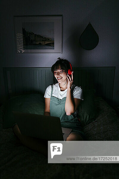Lächelnde Frau mit Kopfhörern und Laptop in der Dunkelkammer