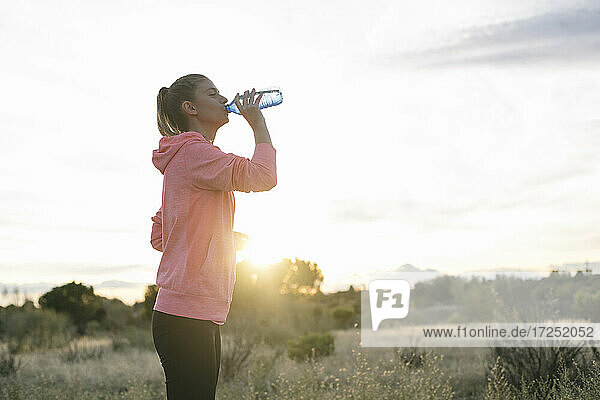 Läuferin trinkt bei Sonnenuntergang Wasser aus einer Flasche