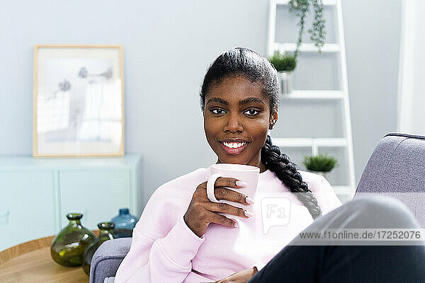 Schöne Frau hält Kaffeetasse beim Entspannen auf dem Sofa zu Hause