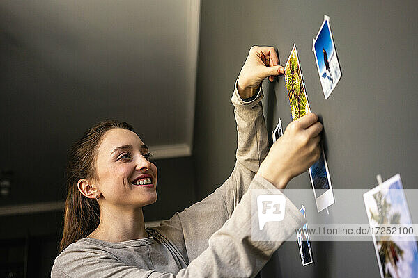 Junge Frau lächelt  während sie zu Hause ein Foto an die Wand klebt