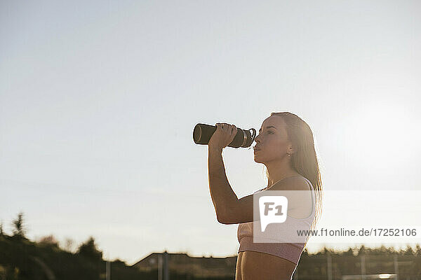 Weibliche Athletin trinkt an einem sonnigen Tag Wasser aus einer Flasche