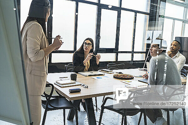 Female entrepreneur discussing with male and female entrepreneurs during meeting at coworking office
