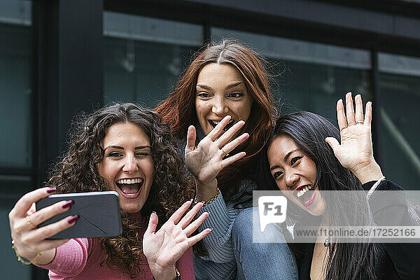 Fröhliche Freunde winken mit der Hand zum Videoanruf auf dem Handy