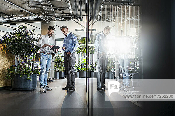 Geschäftsleute  die im Stehen im Büro an einem digitalen Tablet arbeiten