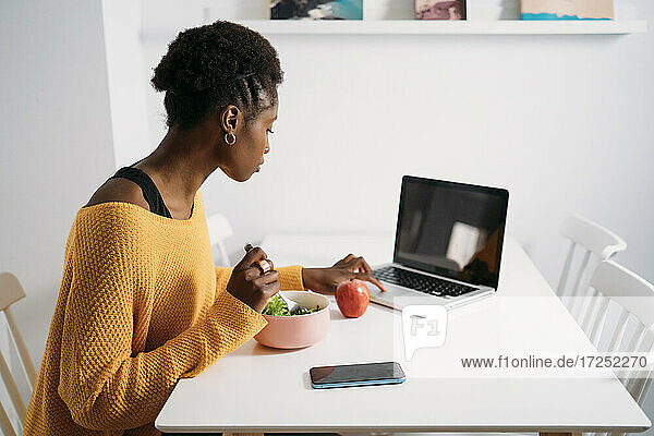 Berufstätige Frau benutzt Laptop beim Frühstück zu Hause
