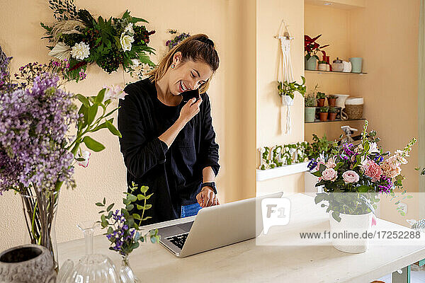 Unternehmerin  die mit einem Smartphone spricht  während sie in einem Workshop einen Laptop benutzt