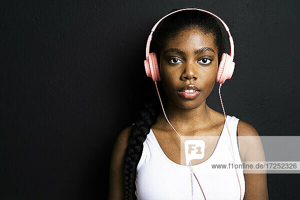 Beautiful woman listening music through headphones against black background