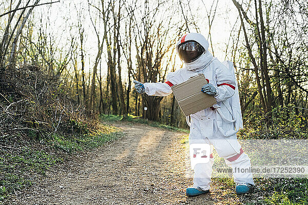 Eine Forscherin im Raumanzug steht mit einem Karton auf einem Feldweg