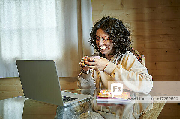 Happy woman having tea in front of laptop at home