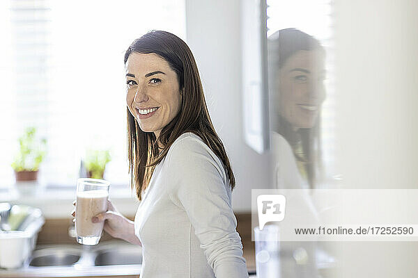 Frau lächelt und hält ein Glas Milchshake in der Küche
