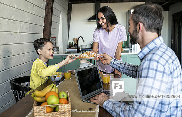Mother serving croissants to family on dining table at home