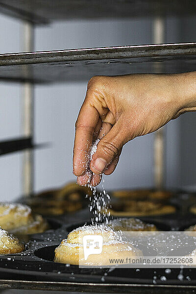 Hand streut Zucker auf Zimtschnecke in der Küche