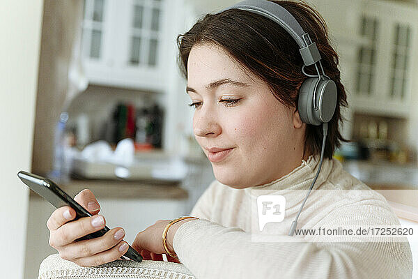 Schöne Frau mit Kopfhörern bei der Benutzung eines Mobiltelefons zu Hause
