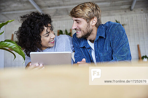 Smiling woman with digital tablet looking at boyfriend at loft