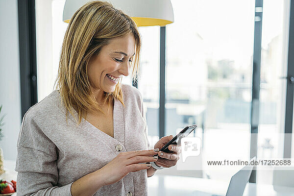 Lächelnde Freiberuflerin  die zu Hause ein Smartphone benutzt
