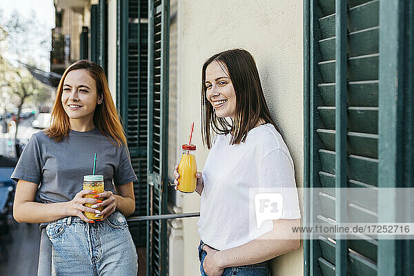 Freundinnen schauen weg  während sie auf dem Balkon Saft trinken