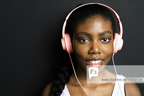 Smiling woman listening music through headphones against black background